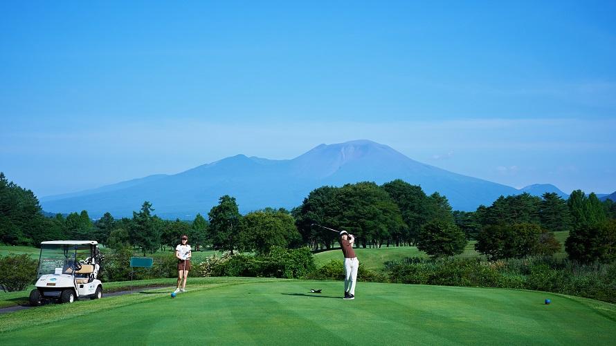 浅間山の景色の前のゴルフコースでティショットを打つゴルファー