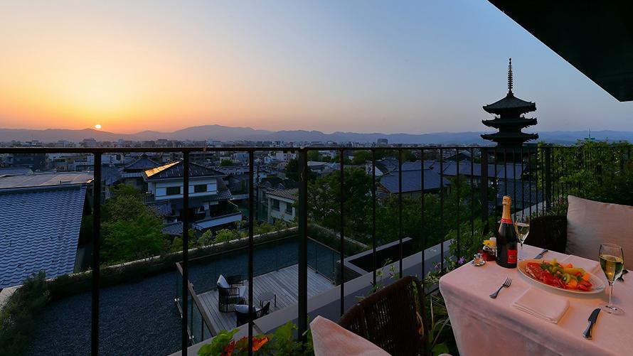 客室パノラミックスイートのテラスから見える、西山に沈む夕日と、テラスのテーブルに並ぶシャンパンとオードブル