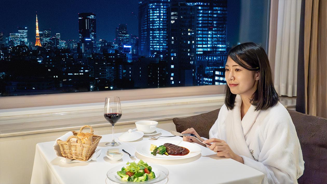 ザ・プリンス さくらタワー東京の「インルームダイニング」で、夜景をバックにディナーを愉しむ女性客。