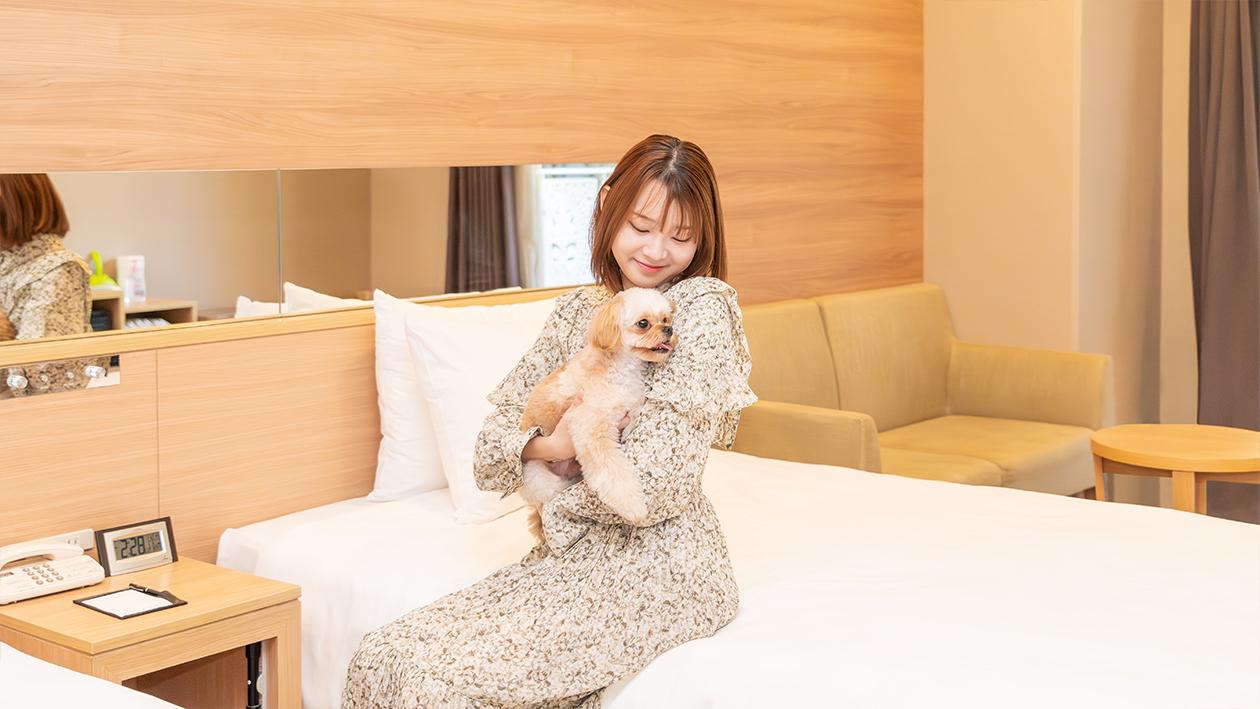 ドッグフレンドリールームで女性がベッドに腰かけながら、犬を抱っこしている。
